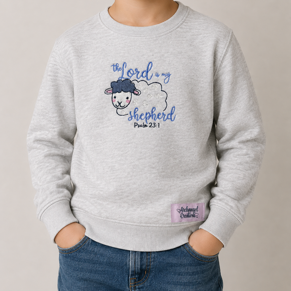 A young boy wearing a light heather gray crewneck sweatshirt with a blue graphic of a sheep and the text 'The Lord is my shepherd Psalm 23:1'.