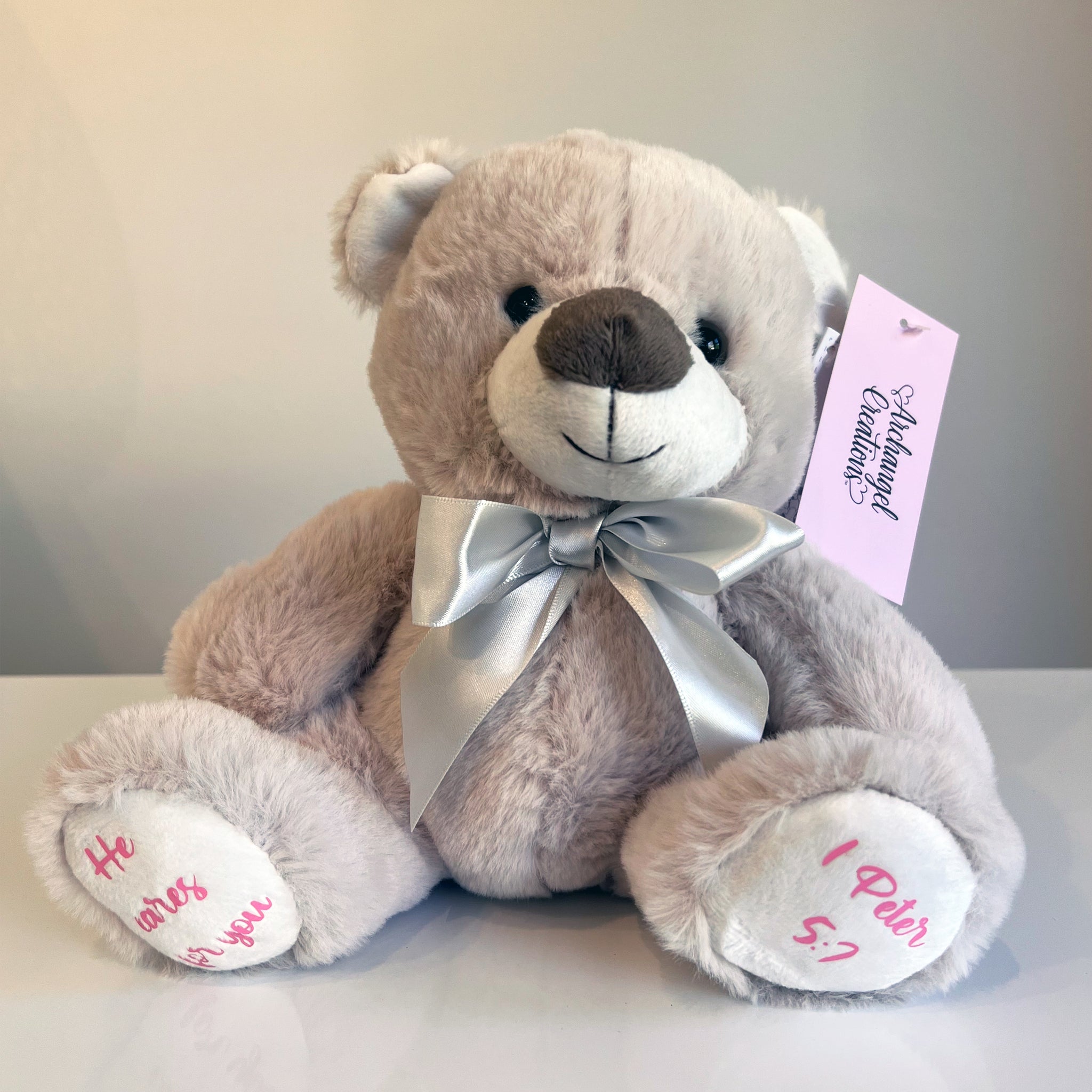 Plush teddy bear with a silver bow, He cares for you Bible verse