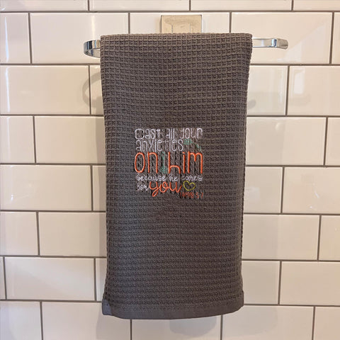 Textured towel with embroidered message hanging on a rack against a tiled wall. bible Verse