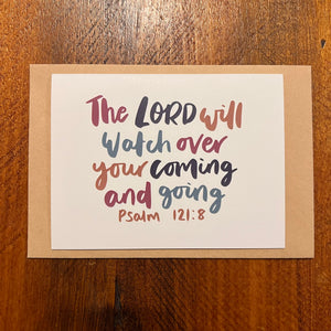 Card with inspirational quote 'The Lord will watch over your coming and going' on a wooden surface