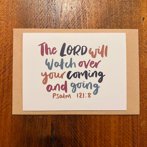 Card with inspirational quote 'The Lord will watch over your coming and going' on a wooden surface