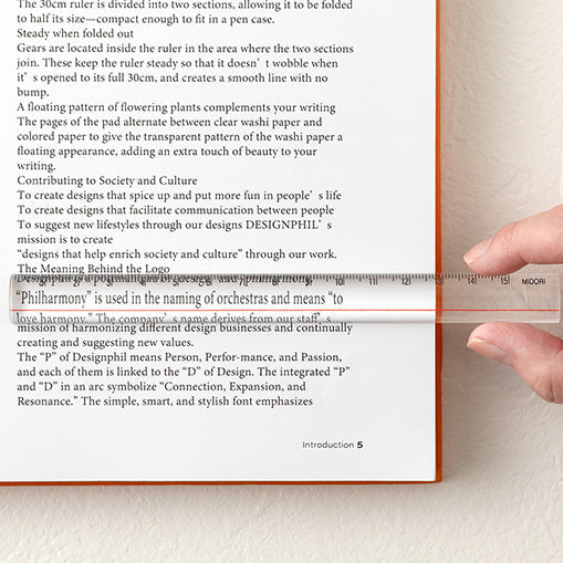 A close-up of a printed book or booklet page with English text, a ruler placed across the page for scale, and Japanese text at the bottom. The ruler appears to be demonstrating the page size or document layout rather than showing a standalone product.